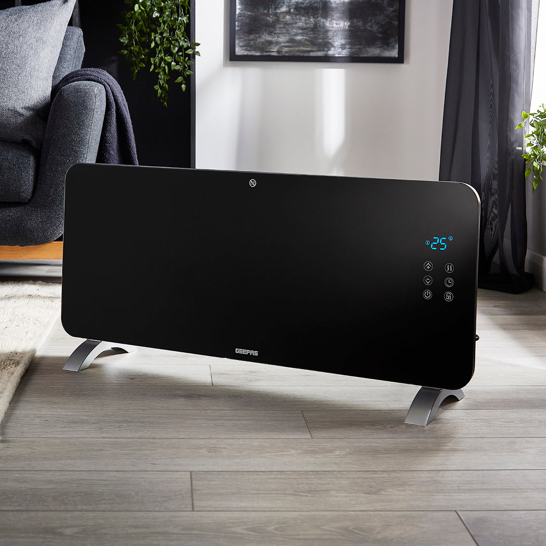 The black electric panel heater in the middle of a living room with different furniture around it such as a sofa, a crème rug and more.