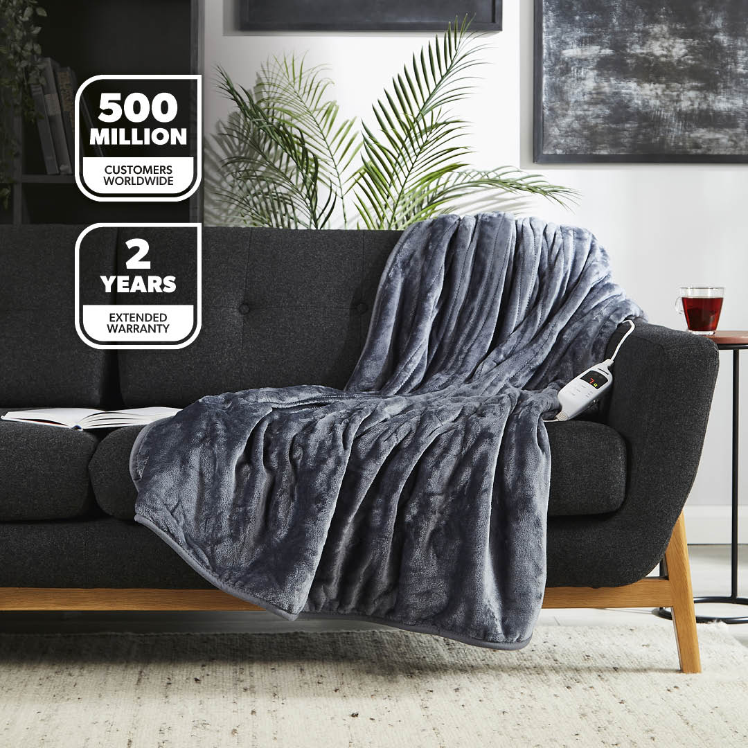 Gray electric blanket draped over a black sofa in a living room setting with warranty information displayed.