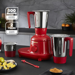 The Geepas red 3-in-1 mixer grinder on a black kitchen countertop with three different grinding jars.