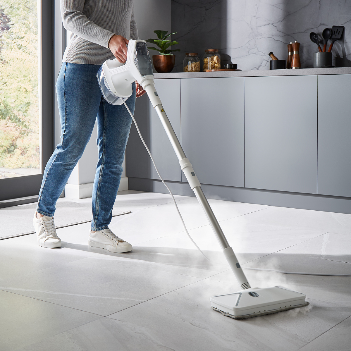 Image shows a person with the electric steam mop and steam cleaner. They are steam cleaning the tiles in the kitchen.