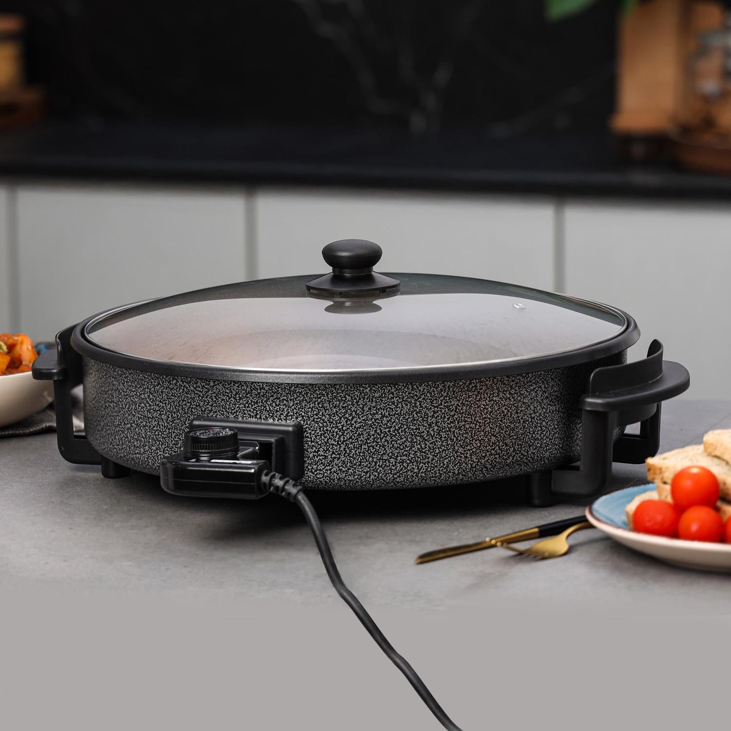 The image shows off the electric wok on top of a kitchen countertop with foods around it.